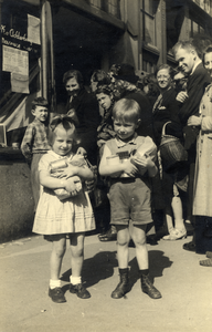 97584 Afbeelding van twee kinderen met hun armen vol etenswaren voor de kruidenierswinkel van de Fa. K. Achterberg ...